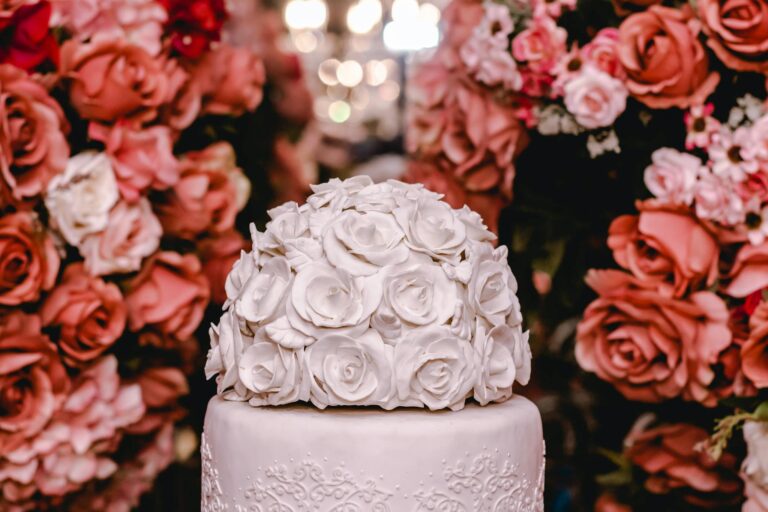 A beautifully decorated white rose cake surrounded by vibrant floral arrangements, perfect for weddings.