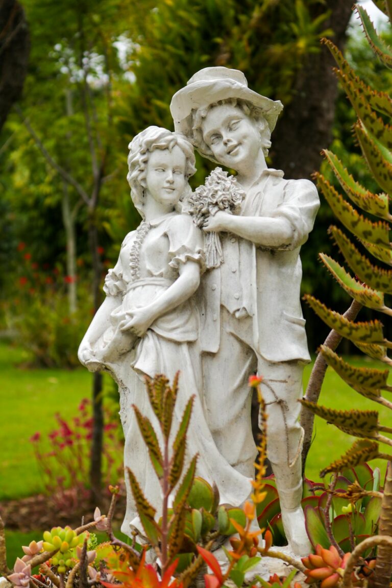 Elegant stone sculpture of a romantic couple surrounded by vibrant garden plants.